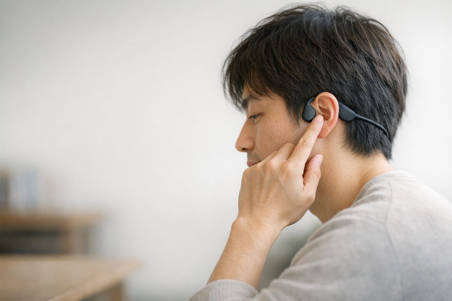 静かな室内で骨伝導イヤホンの音量を控えめに調整する人物(音漏れ配慮のイメージ)